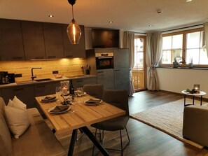 A modern kitchen with dark cabinets, a wooden dining table set for four, and a pendant light.