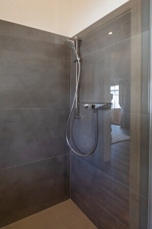 A modern shower with a handheld showerhead, a wall-mounted control panel, and a glass partition.