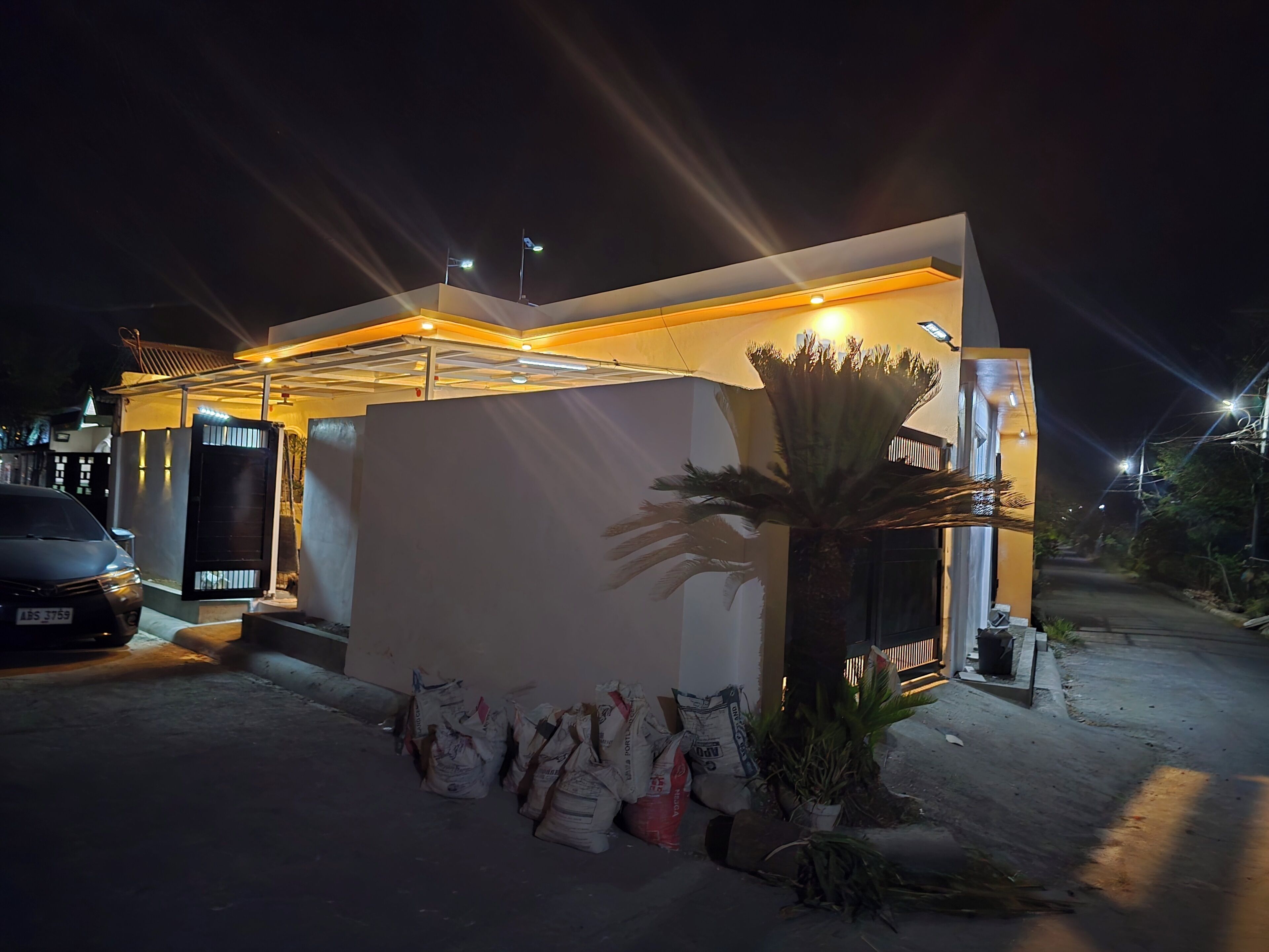 Un edificio moderno con un'auto parcheggiata davanti, una palma e sacchi di materiali.