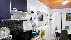 Una cocina moderna con microondas, tostadora y cafetera sobre la encimera. Hay estantes encima de la encimera con varios objetos, y una zona de comedor con sillas y una mesa.