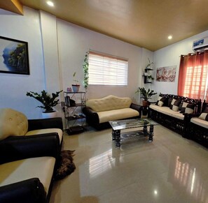 A living room with a sofa, armchairs, a coffee table, a TV, and an air conditioning unit. - Cozy 3-BR house. 15 pax.  Fast WIFI. Near Iloilo airport.  Pet friendly (Zarraga)
