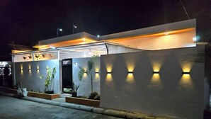 Un edificio moderno con techo plano, entrada protegida por una reja y luces fijadas a la pared.