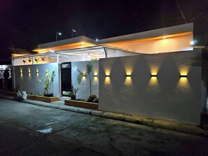 Un bĂątiment moderne dotĂ© dâun toit plat, dâune entrĂ©e sĂ©curisĂ©e par un portail et de luminaires fixĂ©s aux murs.