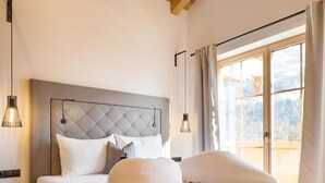Ein Schlafzimmer mit einem großen Bett, Holzbalken an der Decke, einem Nachttisch und einem Fenster mit Vorhängen.
