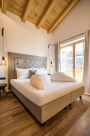 Una camera da letto con un letto grande, travi in legno al soffitto, un comodino e una finestra con tende.