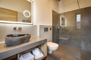 Un bagno moderno con una vasca in pietra, un water e una doccia con pareti in vetro.