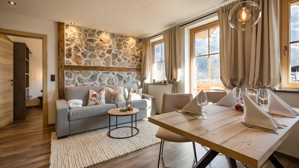 Ein modernes Wohnzimmer mit Steinwand, einer Couch, einem Couchtisch und einem Esstisch für zwei Personen.