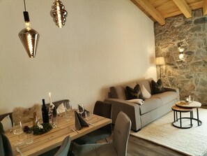 A dining area with a wooden table set for two, a sofa, and a stone wall.