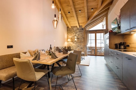 A modern kitchen with wooden beams, a stone wall, and a dining area with a wooden table and chairs.. Apartment "Das Krumerhaus – Die Krumerlodge" with Mountain View, Balcony and Wi-Fi