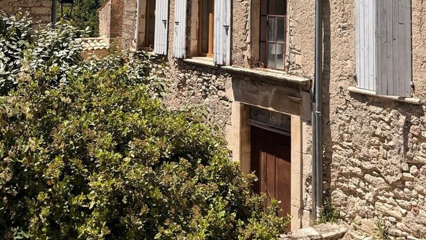 Ein Gebäude aus Stein mit zahlreichen Fenstern und Fensterläden, umgeben von viel Grün.