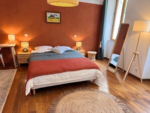 Un dormitorio ordenado con una cama, dos mesitas de noche, una lámpara de pie, una alfombra de fibras naturales y un cuadro en la pared.