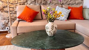 Ein Wohnzimmer mit einer Steinwand, einem Sofa mit orangefarbenen Kissen, einem runden Couchtisch mit Blumen und einer Stehlampe.