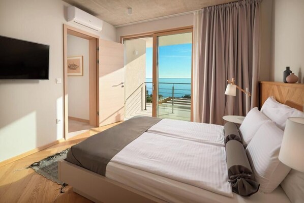 A bedroom with a bed, bedside table, lamp, and a view of the sea through a sliding door. - Villa Bianca Hvar (Sveta Nedjelja)