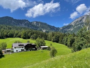 A house with a sloped roof, surrounded by a green field and mountains in the background. - Nusshof Vacation Home for up to 9 people (Berchtesgaden)