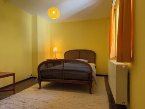A room with a bed, a nightstand, a lamp, a radiator, and a window with curtains. - Nusshof Vacation Home for up to 9 people (Berchtesgaden)