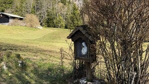 A wooden birdhouse with a white sculpture inside, set in a grassy field with a mountain backdrop. - Nusshof Vacation Home for up to 9 people (Berchtesgaden)