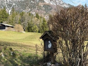 A wooden birdhouse with a white sculpture inside, set in a grassy field with a mountain backdrop. - Nusshof Vacation Home for up to 9 people (Berchtesgaden)