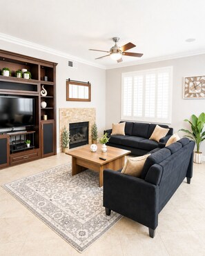 Una sala de estar con televisor, chimenea, sofá, mesa de centro y ventilador de techo.