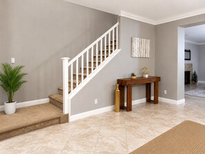 Una escalera con barandillas blancas, una consola decorativa con objetos ornamentales y una planta en maceta.
