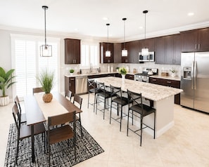 Una cocina moderna con armarios de madera oscura, una isla grande con taburetes de bar, electrodomésticos de acero inoxidable e iluminación colgante.