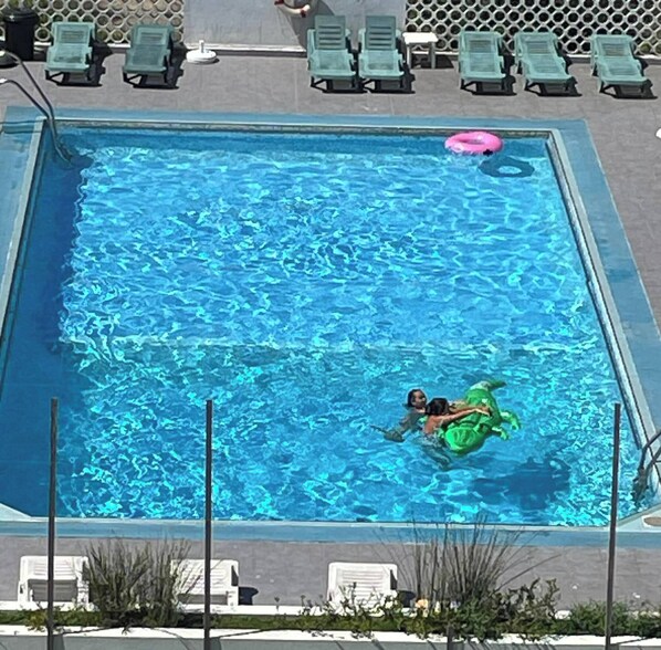 Una piscina rettangolare con acqua cristallina, circondata da lettini e un’area a bordo piscina.