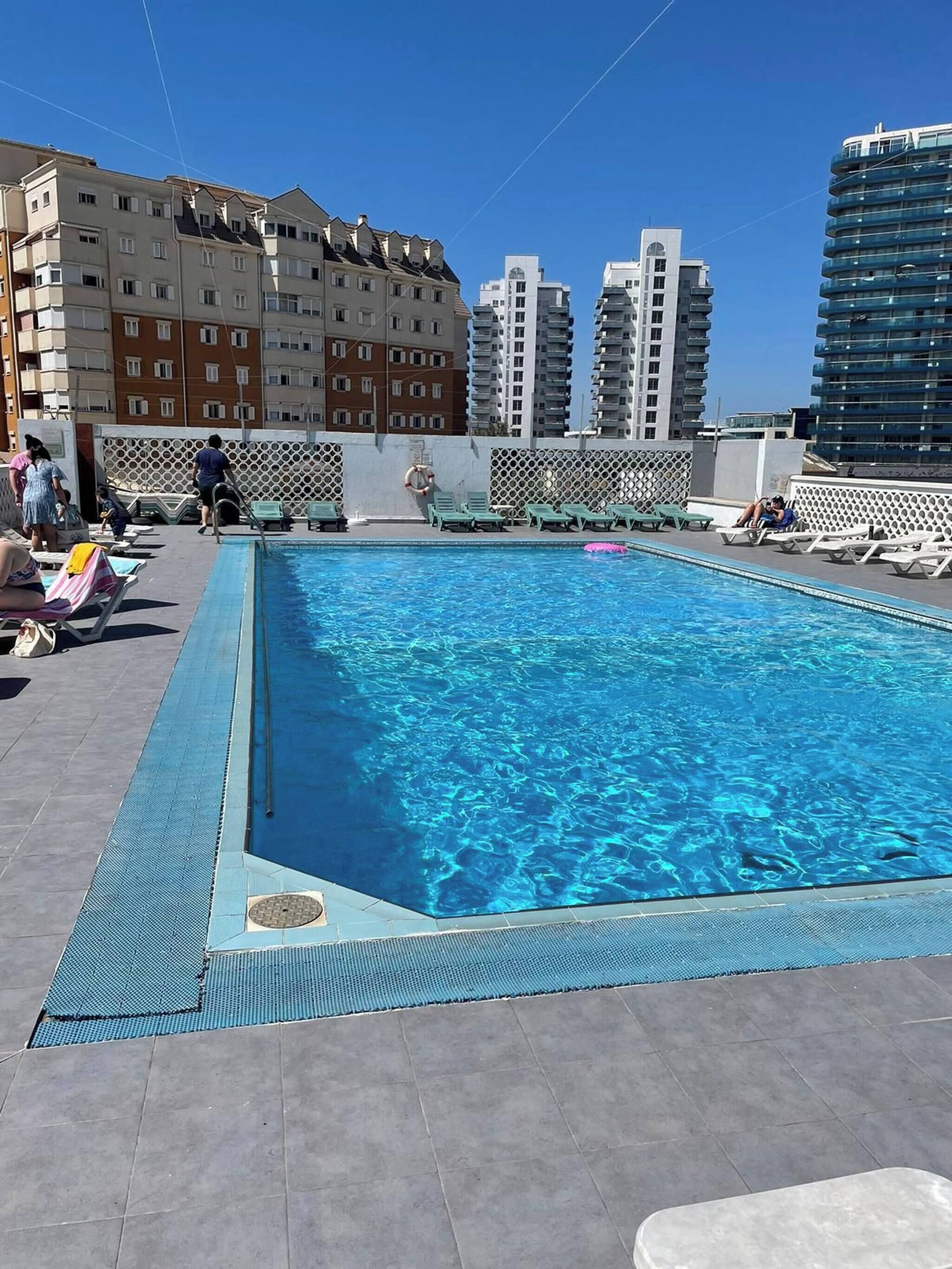 Une piscine sur le toit, dotée de chaises longues, un espace aménagé au bord de la piscine et, en arrière-plan, des immeubles de grande hauteur.