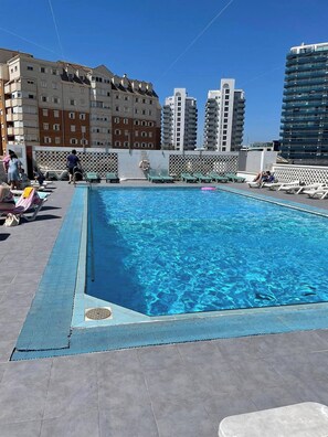 Una piscina sul tetto con poltrone a sdraio, area piscina ed edifici alti sullo sfondo.
