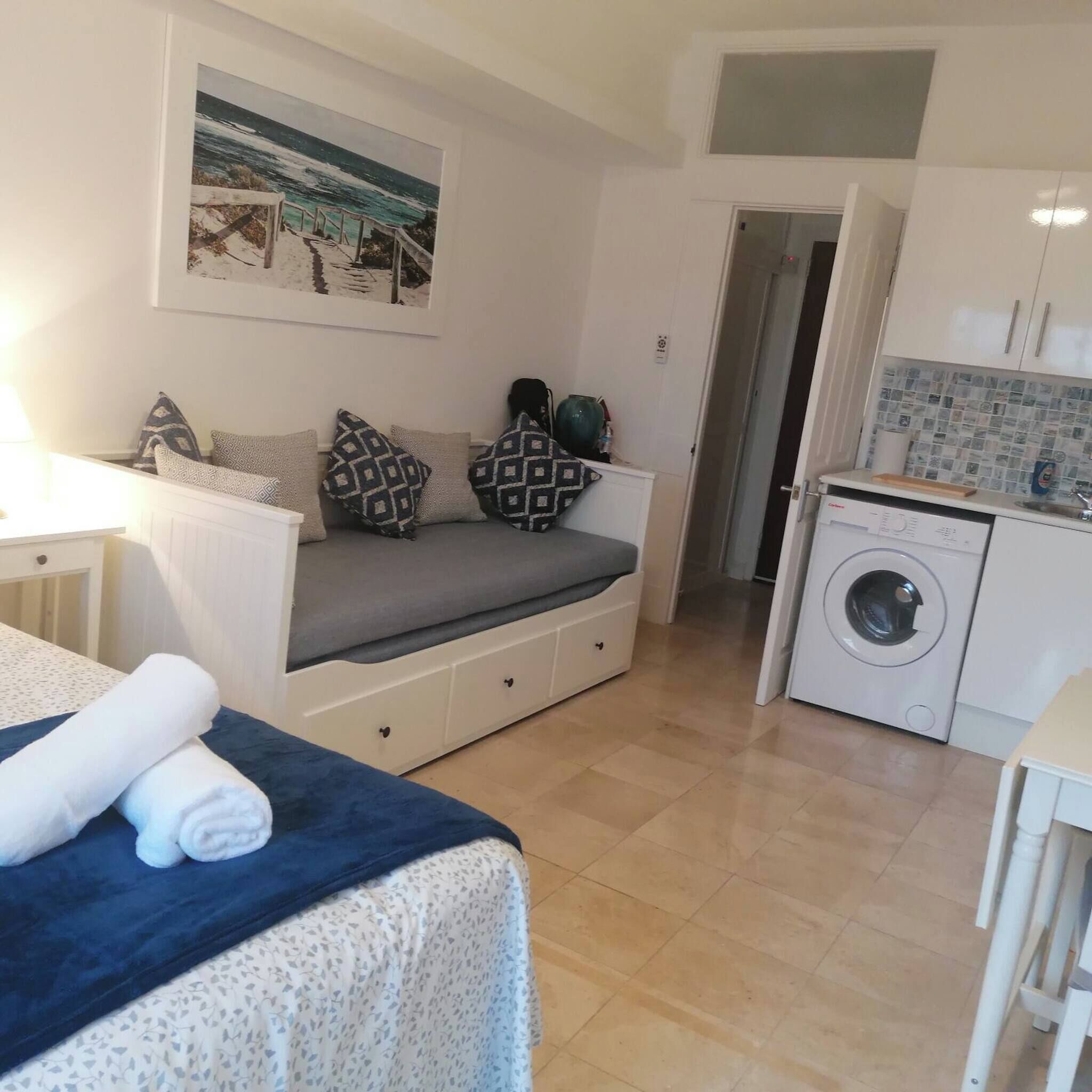 Une pièce de taille modeste comprenant un lit, un canapé, un lave-linge et un coin cuisine.