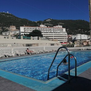 A swimming pool with a metal ladder, lounge chairs, and a building with balconies in the background. - Charming Studio Apartment with Pool Access in Central Gibraltar (Gibraltar)