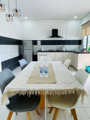 A modern kitchen with a dining area, including a table with chairs, a refrigerator, a stove, and hanging light fixtures. - Oak & Ivory Home • Cozy Clean 3BR • 5km to Airport (Kota Samarahan)