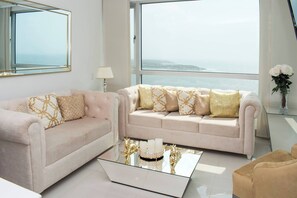 Ein modernes Wohnzimmer mit zwei Sofas, einem Glastisch und Meerblick.