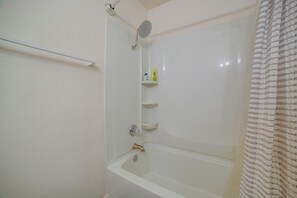 Une salle de bain Ă©quipĂ©e dâune baignoire, dâune douche et dâune Ă©tagĂšre oĂč sont rangĂ©s les articles de toilette.