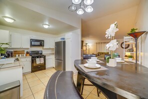 Une cuisine moderne avec des meubles blancs, un four à micro-ondes, une cuisiniÚre et un réfrigérateur. On y trouve une table à manger avec un banc et une plante en pot.