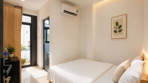 Une chambre à coucher comprenant un lit, un bureau, un climatiseur et une porte donnant sur un balcon.