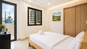 Une chambre d’hôtel comprenant un lit, une armoire, un bureau avec une bouilloire et une fenêtre donnant sur des immeubles.