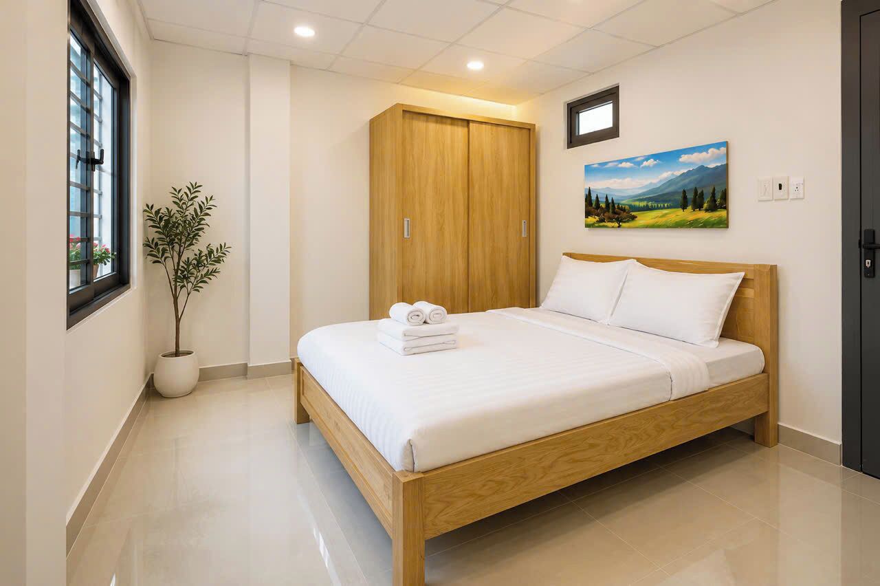 A neatly made bed with white linens, a wooden wardrobe, a potted plant, and a landscape painting on the wall.