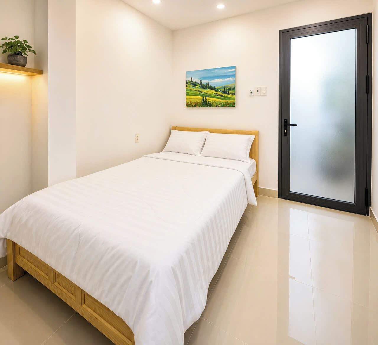 A bedroom with a bed, a door, a wall-mounted painting, and a potted plant.