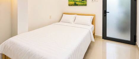A bedroom with a bed, a door, a wall-mounted painting, and a potted plant.