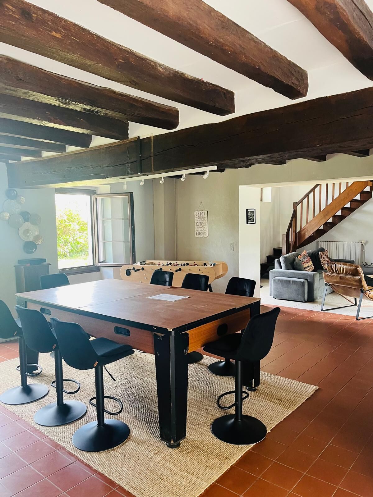 A spacious room with a wooden table and chairs, a foosball table, a sofa, and a staircase.