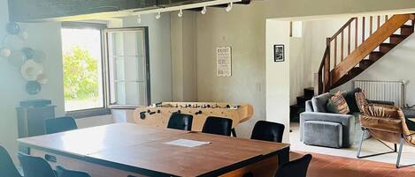 A spacious room with a wooden table and chairs, a foosball table, a sofa, and a staircase.