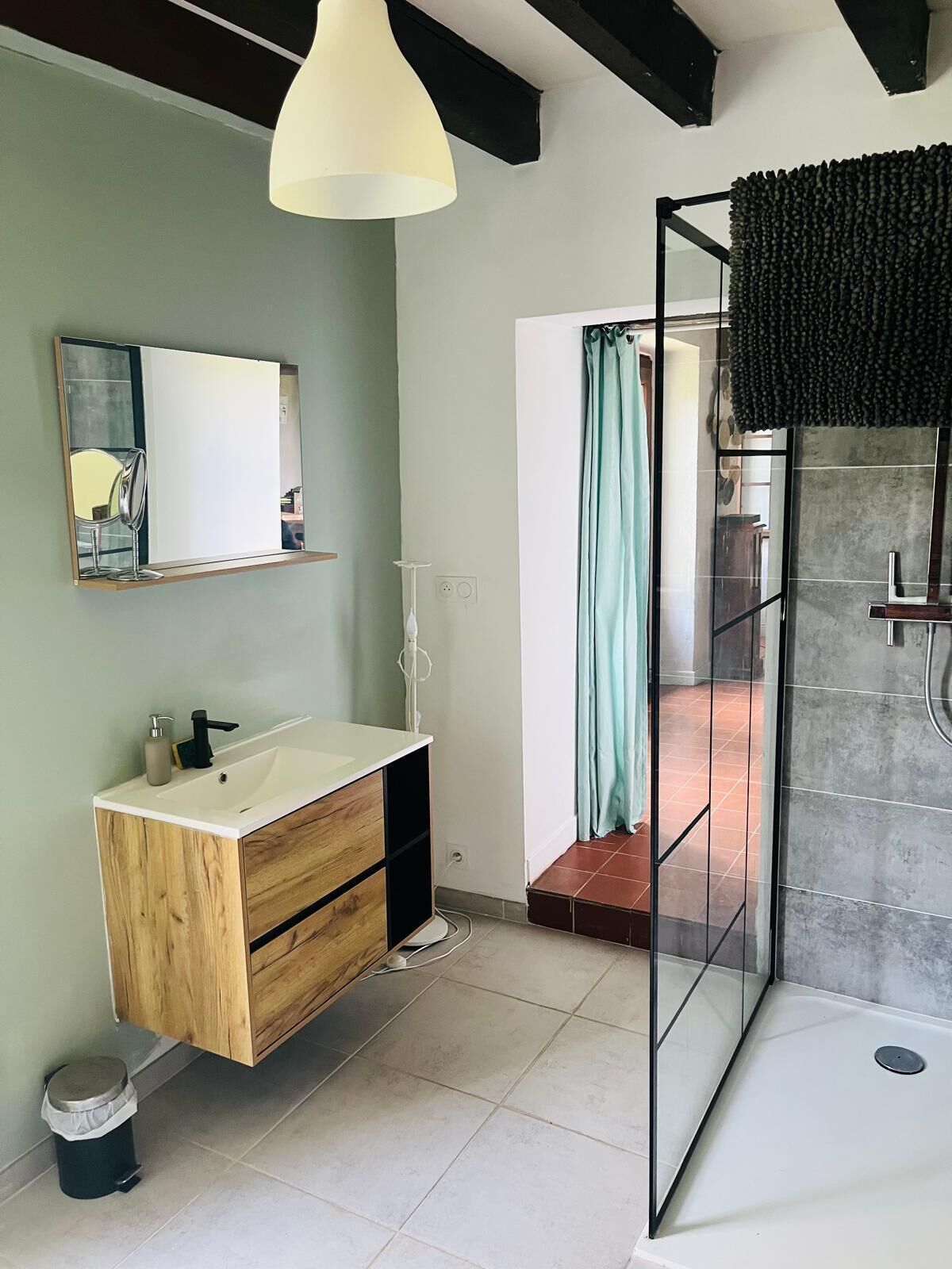 A modern bathroom with a wooden vanity, a mirror, a shower with a glass door, and a hanging light fixture.
