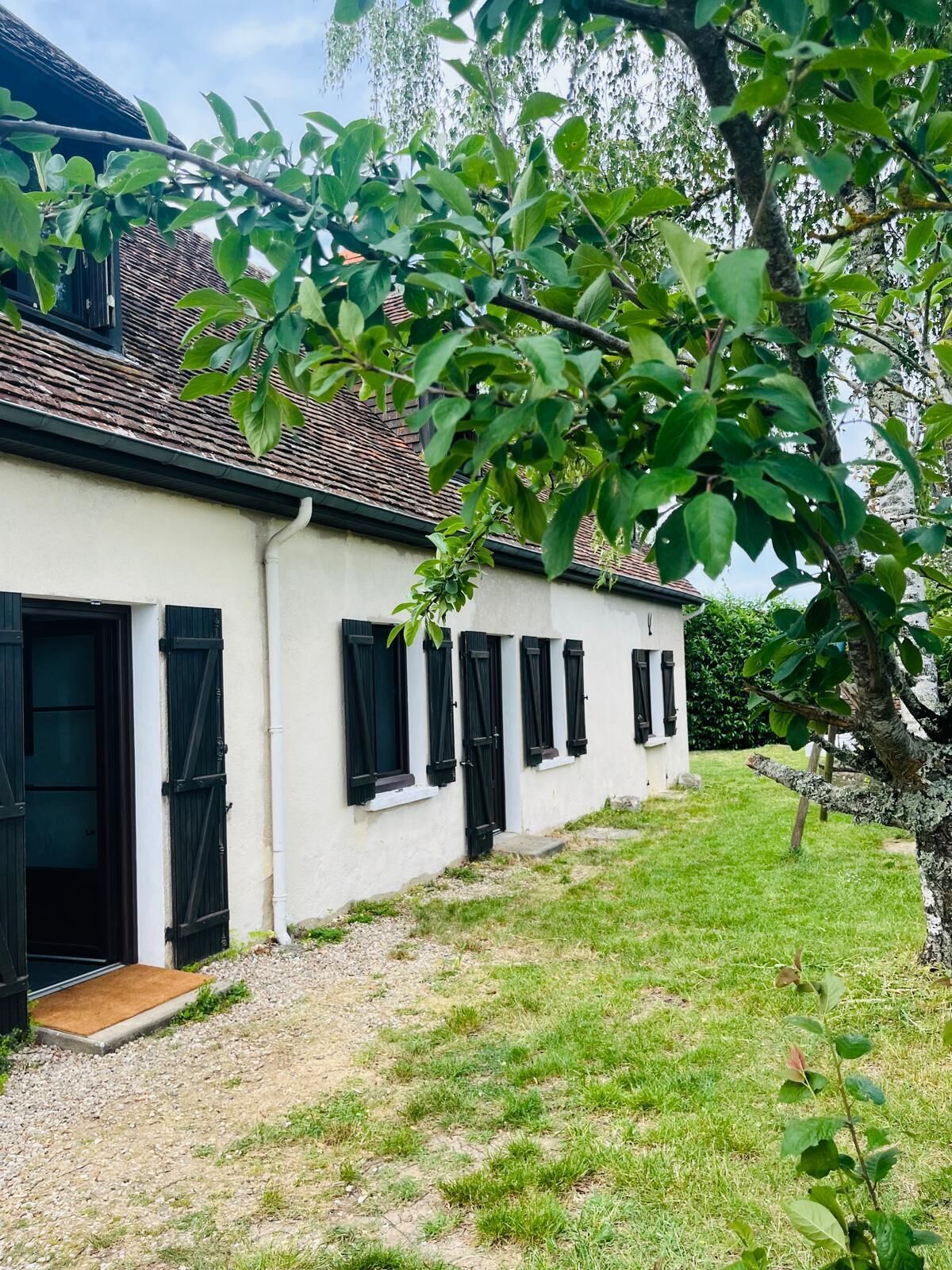 A white building with black shutters, a tiled roof, and a grassy yard.