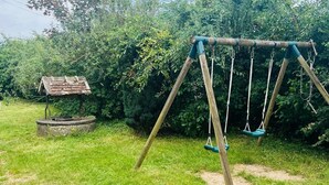 Eine Schaukel auf einem Rasen mit einer rustikalen Holzkonstruktion und dichtem Grün im Hintergrund.