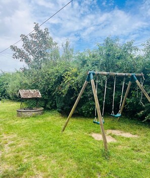 En gunga placerad på en gräsig gård, med en rustik träkonstruktion och tät lövverk i bakgrunden.