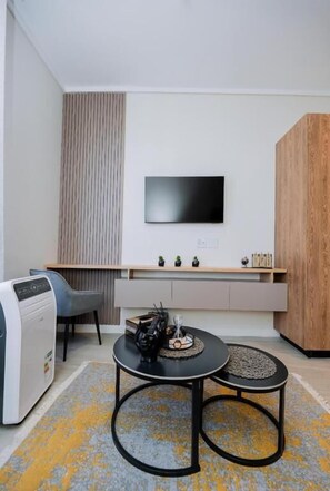 Een moderne woonkamer met een flatscreen televisie aan de muur, een bank, een salontafel en een klein kastje onder de televisie.