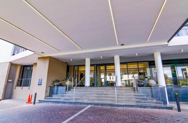 Una entrada de hotel moderna con fachada de vidrio, una escalera que conduce al vestíbulo y un suelo empedrado de ladrillo.