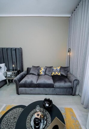 A modern living room with a grey sofa, a coffee table, and a lamp. - Trilogy studio apartment 831 (Pretoria)