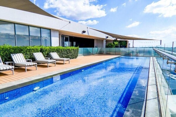 A modern pool area with lounge chairs, a clear view of the sea, and a contemporary building with large windows. - Trilogy studio apartment 831 (Pretoria)