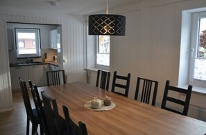 Een eethoek met een houten tafel, zwarte stoelen, een geweven placemat en een hanglamp.