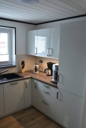 Une cuisine compacte avec des meubles blancs, un plan de travail en bois, une machine à café et un bloc à couteaux.